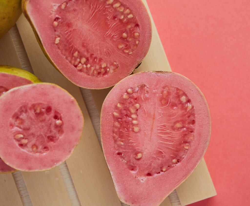 close-up of a fresh guava cut in half, the pink color of the pulp matches the background.